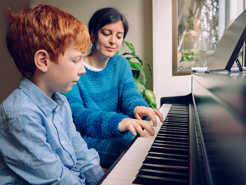 A woman teaches the child what is the proper hand placement in piano instrument.