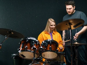 A man teaches the girl on how to play the drum instrument.