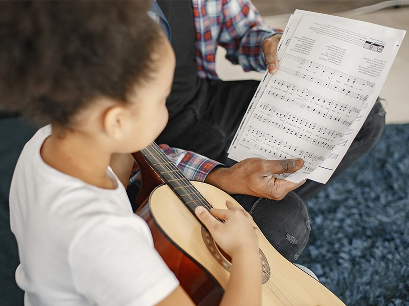 Father with daughter on couch. Girl holding a guitar. Learning guitar By Music School In Oak Park.