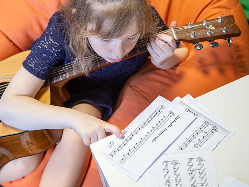 A little girl with a guitar learns solfeggio, sheet music and music theory Music School In Oak Park.