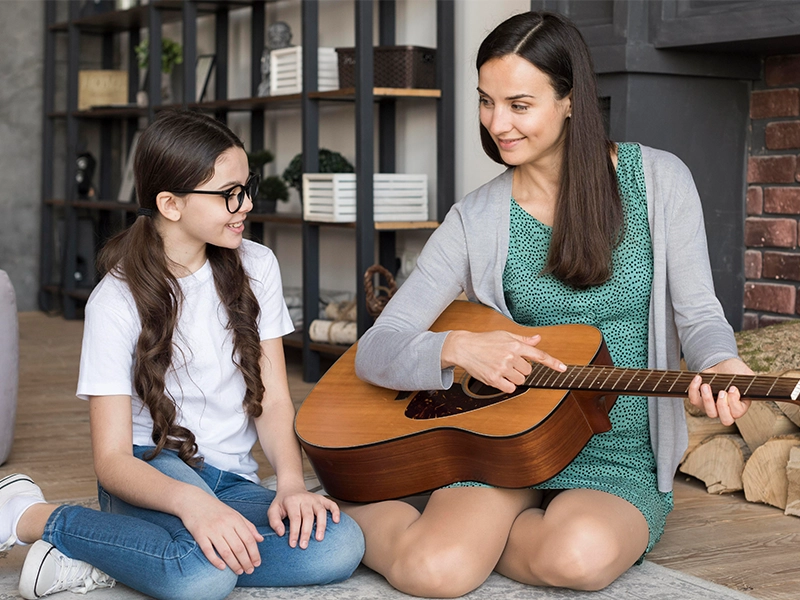 Mother teaching girl to play guitar By Music School In Hollywood.